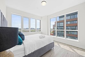 Un dormitorio moderno con una cama grande, amplias ventanas y vistas a la ciudad.