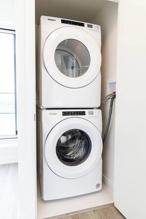 Eine gestapelte Waschmaschine und ein Trockner in einem Waschraum mit einem Fenster darüber.