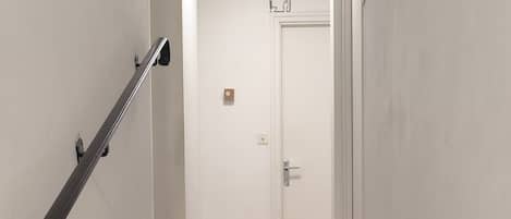 Una escalera con barandilla que conduce a una puerta, con un interruptor de luz encima.