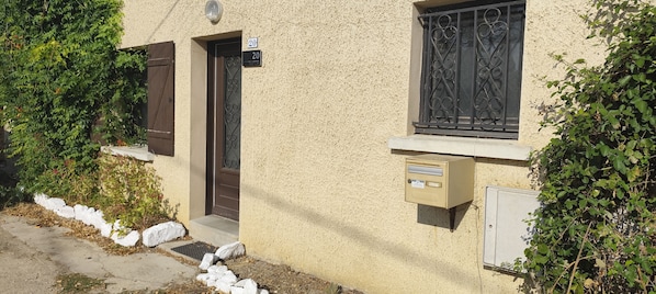 A building with a beige stucco exterior, a brown door, and a window with decorative iron bars. - Spacious House in the Peaceful Countryside (Val-Sonnette)
