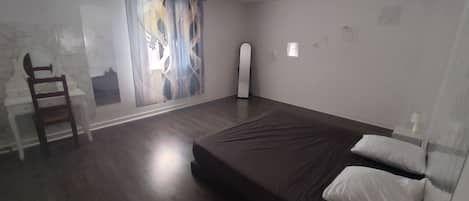A bedroom with a bed, a chair, a mirror, and a window with a view.