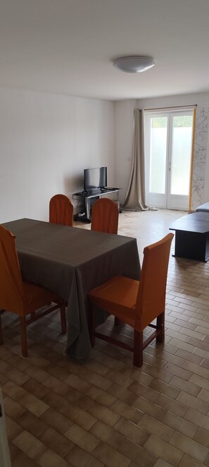 Ein Essbereich mit Tisch und Stühlen, einem Fernseher auf einem Schrank und einem Fenster mit Vorhängen.