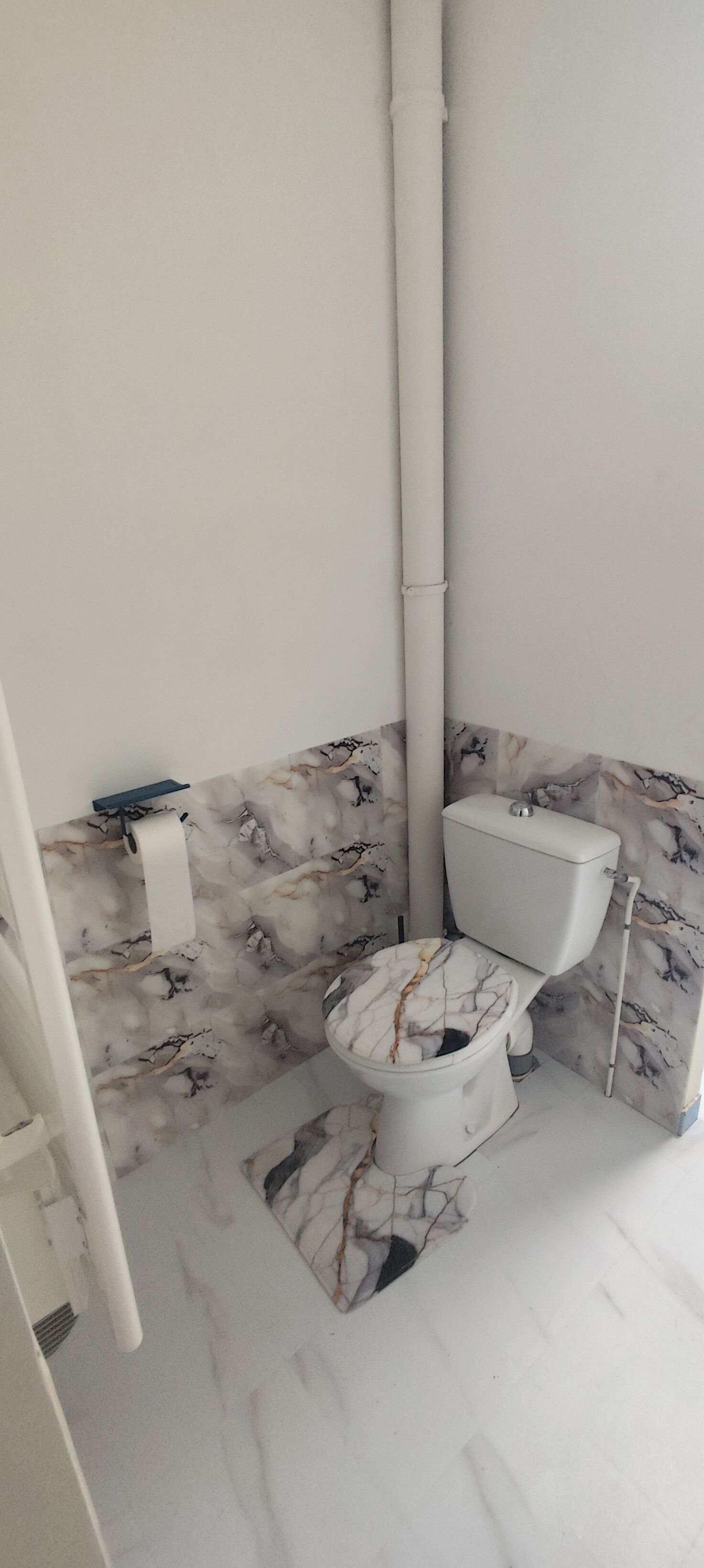 Un baño con inodoro, paredes con diseño de mármol y piso blanco.