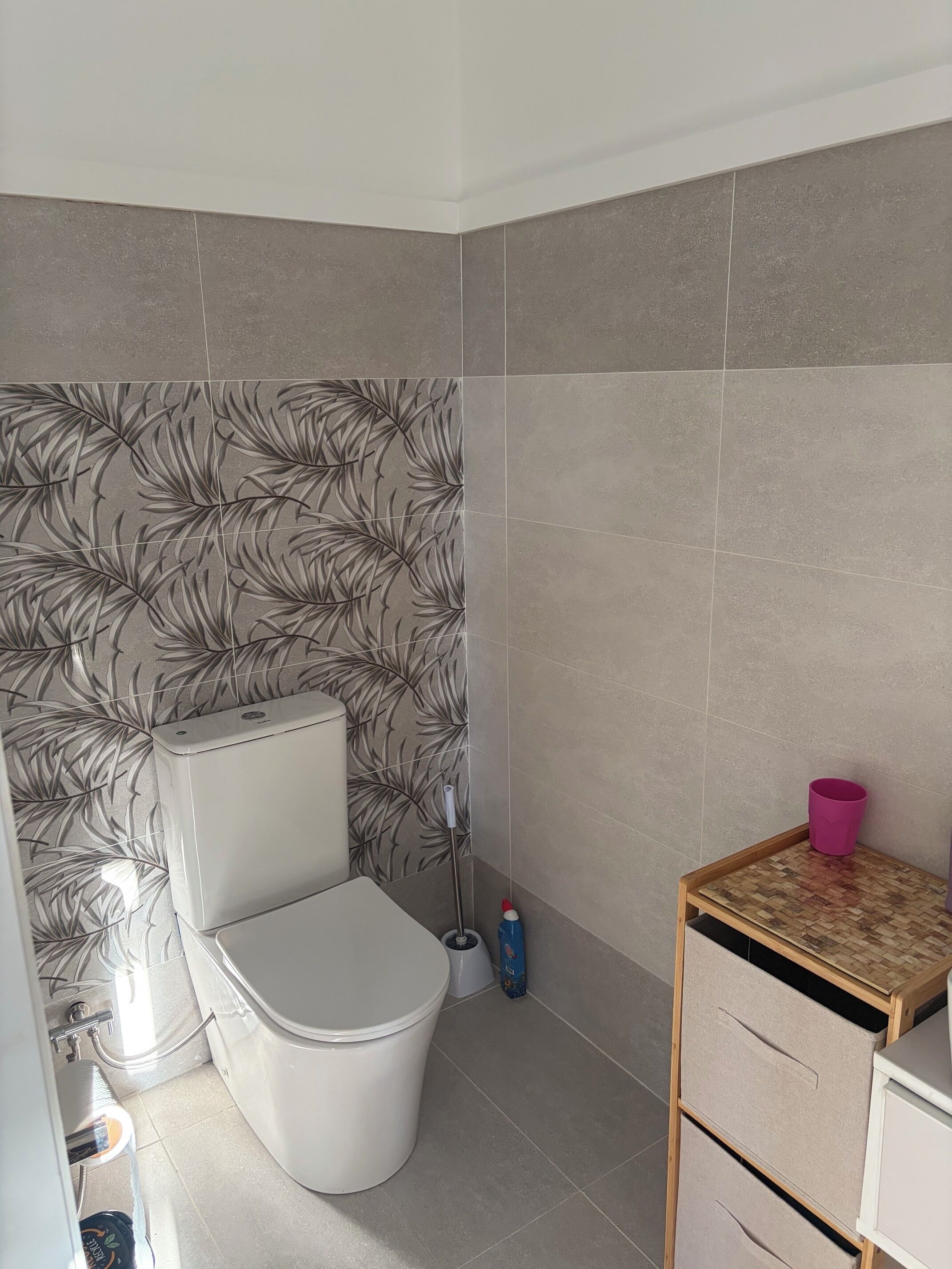 Un bagno con il water, un bidet, un piccolo tavolino con una tazza rosa e una parete decorata con un motivo a foglia.