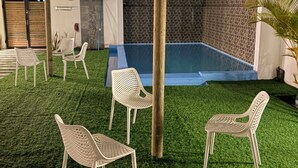 Ein Außenbereich mit Schwimmbad, Kunstgrashaus und weißen Kunststoffstühlen.