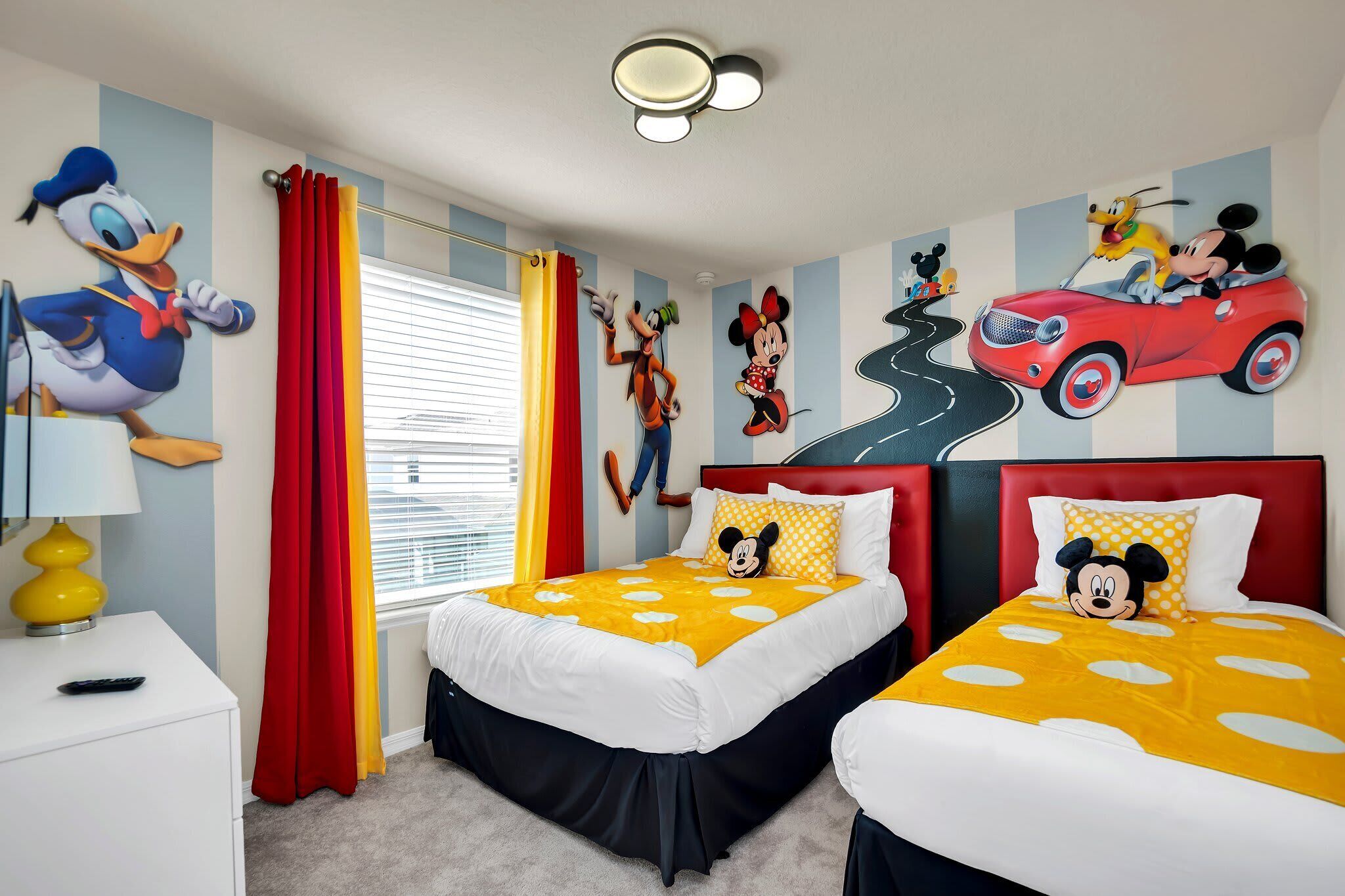Un dormitorio infantil con dos camas, un cojín de Mickey Mouse y un mural con personajes de Disney.
