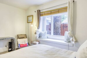 A bedroom with a bed, a bedside table with books, a lamp, and a window with curtains. - Gardner Mountain Hideaway (South Lake Tahoe)