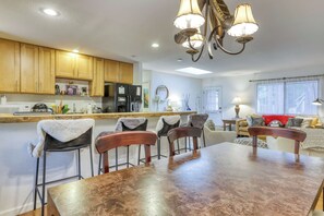 A modern kitchen with wooden cabinets, a dining table with chairs, a chandelier, and a living area with a sofa and a window. - Gardner Mountain Hideaway (South Lake Tahoe)