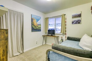 Ein Schlafzimmer mit einem Bett, einem Fernseher auf einem Tisch, einem Poster an der Wand und einem Fenster mit Vorhängen.