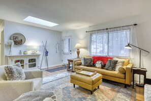Ein Wohnzimmer mit einer Couch, einem Sessel, einem Hocker, einem Kamin und einem großen Fenster mit Jalousien.
