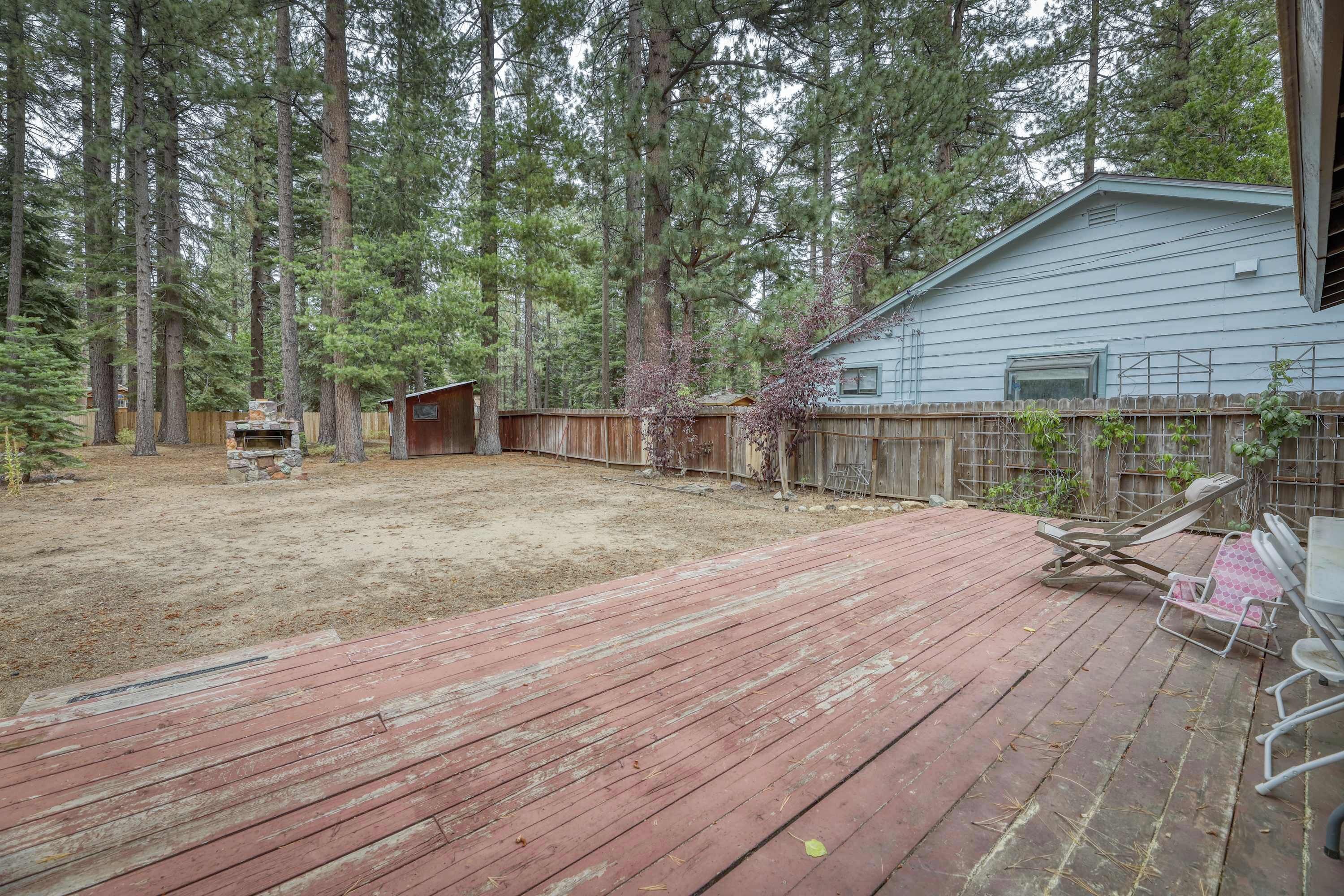 A backyard with a wooden deck, a stone fireplace, and a wooden fence.