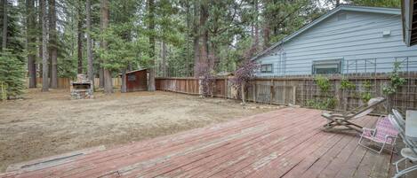 A backyard with a wooden deck, a stone fireplace, and a wooden fence.