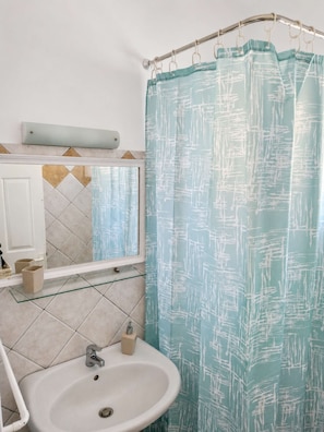 A bathroom with a white sink, a mirror, and a shower curtain with a white abstract pattern. - Sea View Studios in Syros – Litus Studios (Syros)