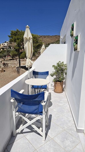 A small outdoor balcony with a white table and blue chairs, a potted plant, and a view of the landscape. - Sea View Studios in Syros – Litus Studios (Syros)