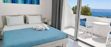 A hotel room with a bed, a view of the sea, and a balcony with a table and chairs.
