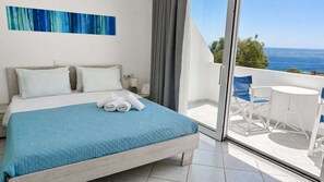 A hotel room with a bed, a view of the sea, and a balcony with a table and chairs. - Sea View Studios in Syros – Litus Studios (Syros)