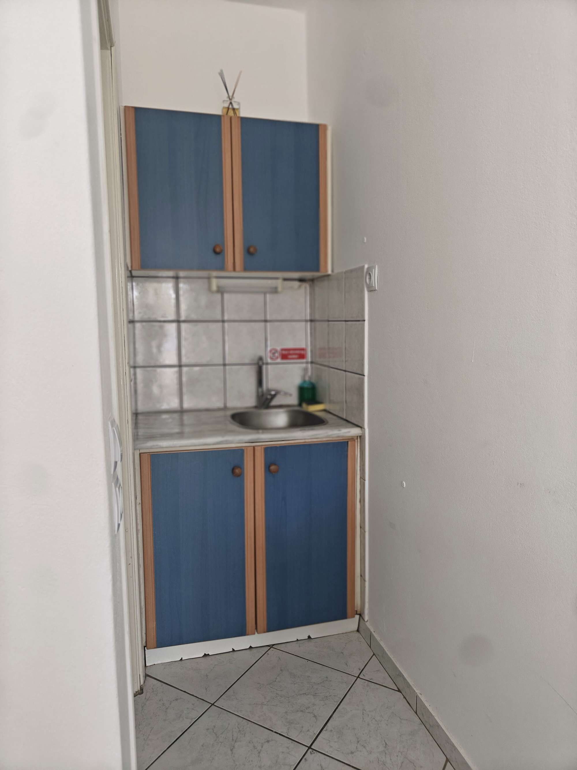 Eine kleine Küche mit blauen Schränken, einem Edelstahlspülbecken und Fliesenboden.