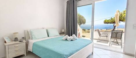 A bedroom with a bed, bedside tables, a nightstand, a view of the sea, and a balcony with chairs.