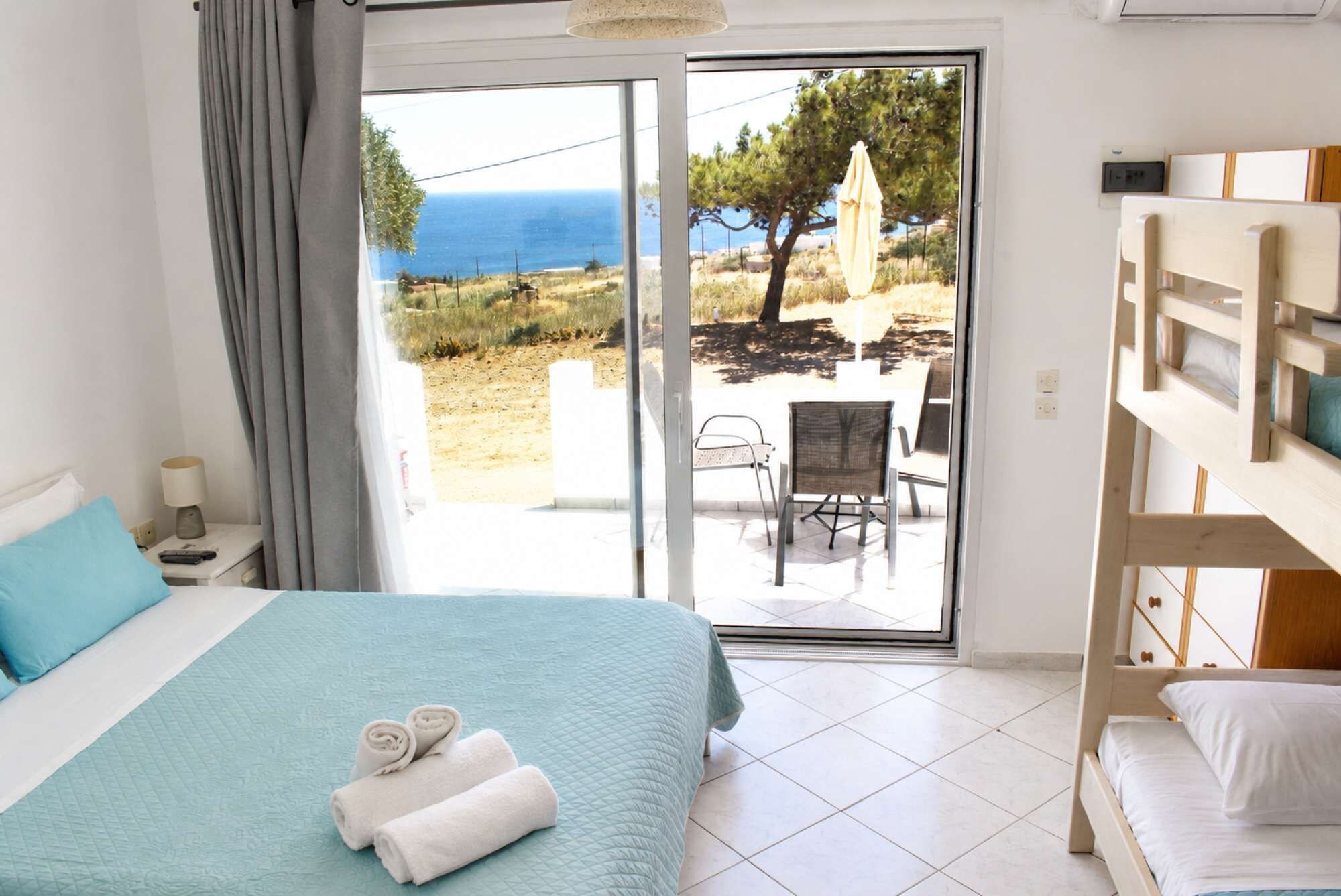 A bedroom with a bed, a wooden bunk bed, a balcony with a view of the sea, and a chair.