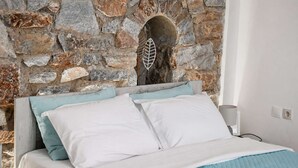 Een bed met wit en lichtblauw beddengoed, een stenen muur met een boog en een lamp op het nachtkastje.