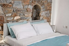 A bed with white and light blue bedding, a stone wall with an archway, and a lamp on the bedside table. - Sea View Studios in Syros – Litus Studios (Syros)