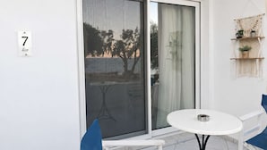 Een balkon met een schuifdeur, een klein rond tafeltje, twee stoelen en een macramé wanddecoratie.