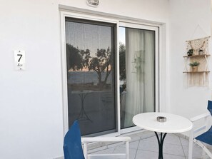 A balcony with a sliding glass door, a small round table, two chairs, and a macrame wall hanging. - Sea View Studios in Syros – Litus Studios (Syros)