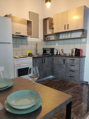 A kitchen with a dining table, a wine glass, and various kitchen appliances. - Sea View Studios in Syros – Litus Studios (Syros)