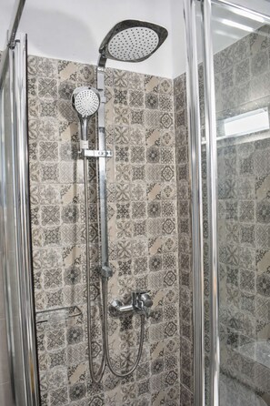 A shower with a handheld showerhead and a wall-mounted rain showerhead, both with multiple nozzles. - Sea View Studios in Syros – Litus Studios (Syros)