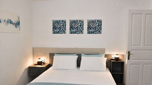 Quarto de hotel com cama, duas mesas de cabeceira com luminárias, uma porta e três obras de arte fixadas na parede.
