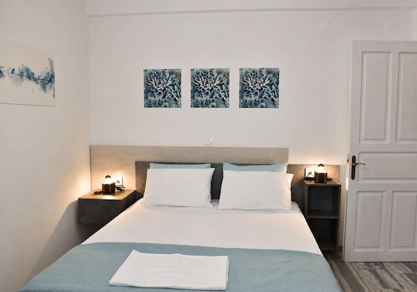 A hotel room with a bed, two bedside tables with lamps, a door, and three wall-mounted artworks. - Sea View Studios in Syros – Litus Studios (Syros)