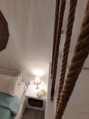 Een slaapkamer met een bed, een nachtkastje met een lamp en een touw aan de muur.