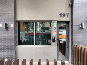 Une entrée d’immeuble avec une porte en verre, le numéro « 197 » au-dessus, et un panneau indiquant l’entrée pour les visiteurs.