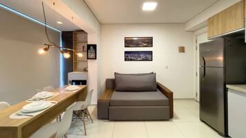 A compact living space with a dining area, a sofa bed, a refrigerator, and wall-mounted artwork.