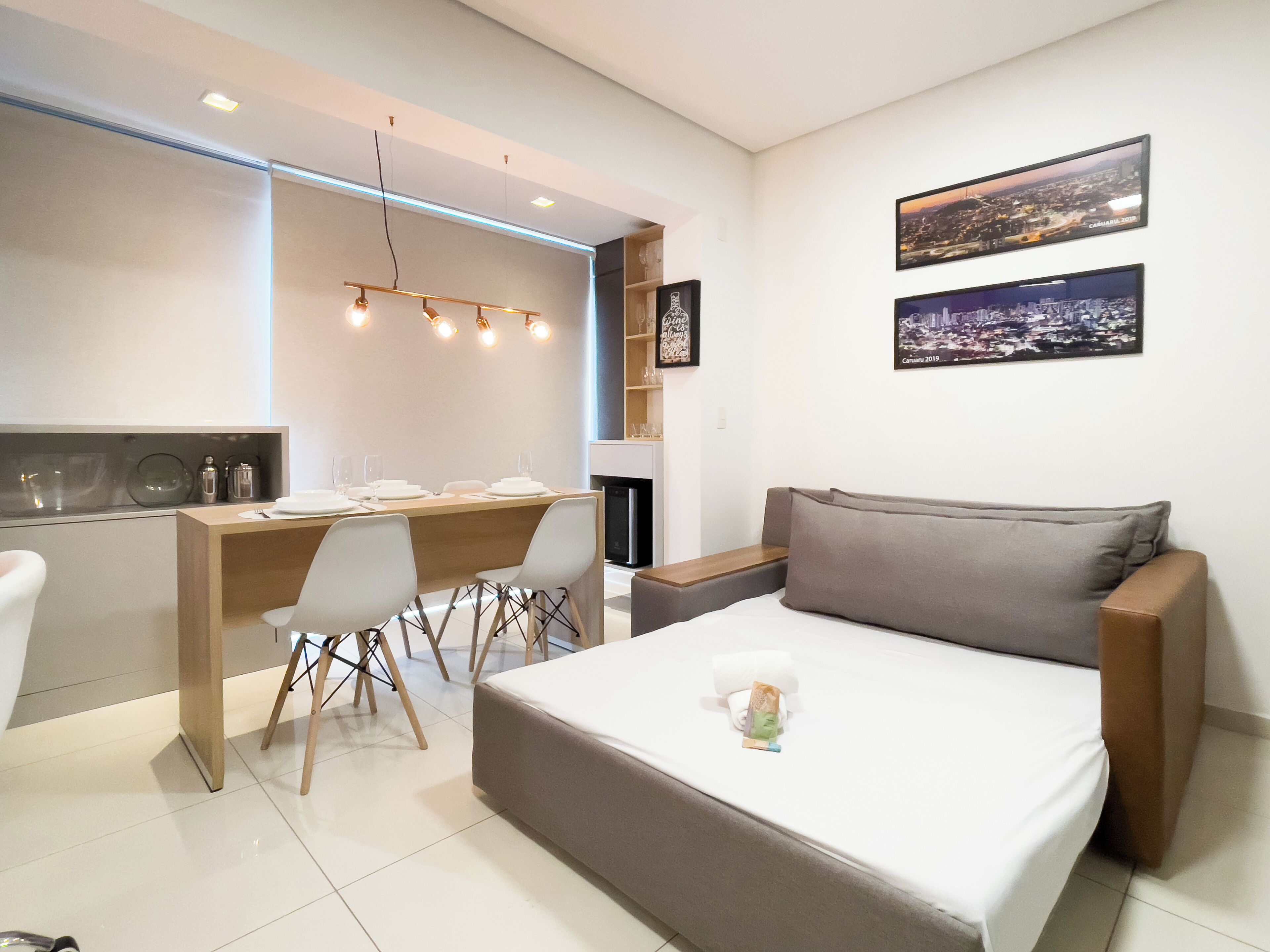Quarto de hotel moderno com uma cama, uma escrivaninha e uma cadeira. Há duas molduras na parede.