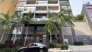 A multi-story building with balconies, palm trees, and a gated entrance. - Genebra (São Paulo)