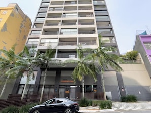 A multi-story building with balconies, palm trees, and a gated entrance. - Genebra (São Paulo)