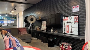 A modern interior with a black brick wall, a flat-screen TV, a sofa, and a wall-mounted shelf with various items. - Genebra (São Paulo)