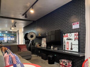 A modern interior with a black brick wall, a flat-screen TV, a sofa, and a wall-mounted shelf with various items. - Genebra (São Paulo)