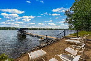 Une terrasse au bord du lac, dotée de chaises longues, une jetée avec un bateau, et une vue dégagée sur le lac et les arbres.