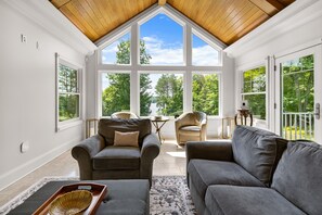 A sunlit room with a sloped ceiling, large windows, a grey sofa, two armchairs, and a small table with a decorative tray. - ‘Reel’ Relaxing Luxury Retreat on Pike Lake (Duluth)