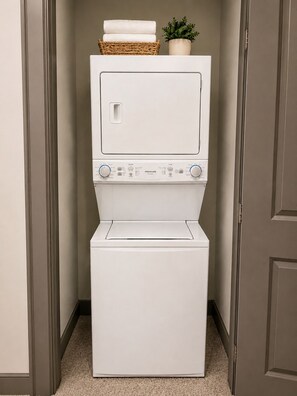 A front-loading white washer and dryer unit with control knobs and a basket of folded towels on top. - Stylish 1-bedroom in Midtown Atlanta-Across From Mercedes Benz Stadium (Atlanta)