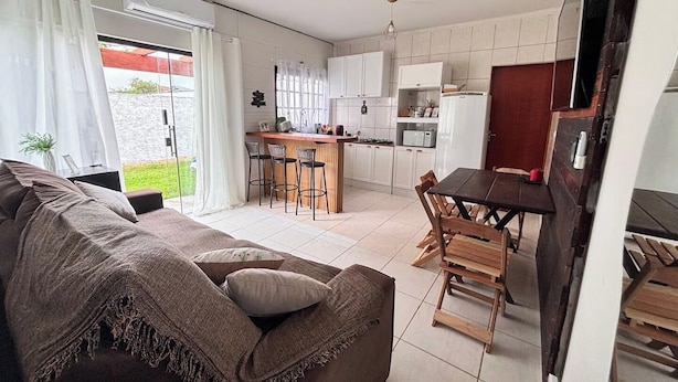 A modern living room with a sofa, a dining table with chairs, and a kitchen area with cabinets and appliances. - Complete private house - Air conditioning. Wi-Fi - 3 bedrooms (Ilha Comprida)