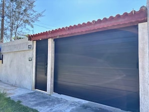 A garage with a closed dark roller door, a concrete wall with a number sign, and a red roof.