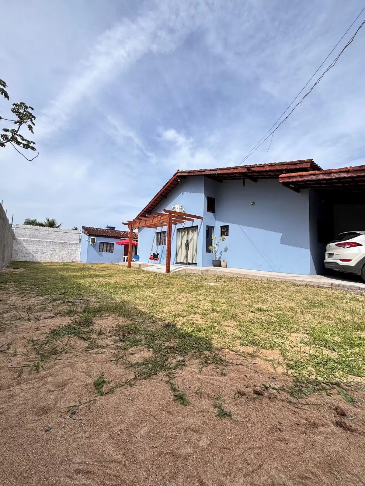 Um imóvel residencial com fachada azul, um alpendre coberto e um carro branco estacionado na entrada.
