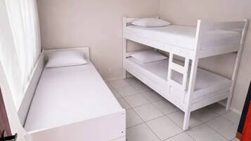Quarto com beliche, uma cama de solteiro, janela com cortinas e ventilador de teto.