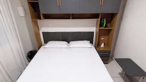 A bed with a grey headboard, a wooden shelf above, and a small bedside table with a lamp. - Complete private house - Air conditioning. Wi-Fi - 3 bedrooms (Ilha Comprida)