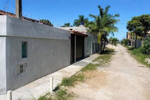A narrow concrete pathway flanked by a high wall with a barred top, leading to a building with a metal door and a small window.