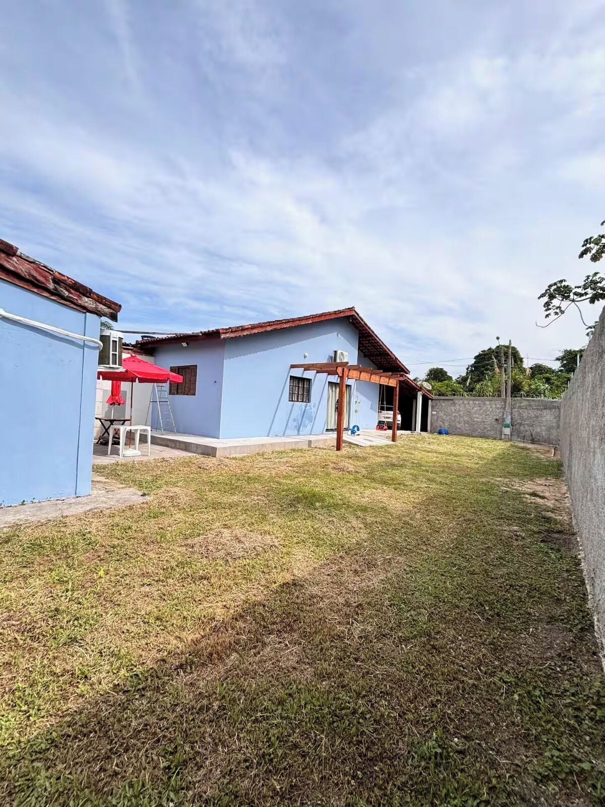 Uma propriedade residencial com fachada azul, pérgola de madeira e gramado.