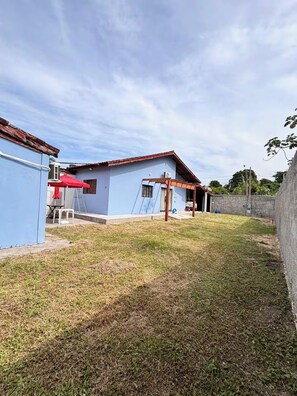 Una propietat residencial amb façana blava, una pèrgola de fusta i un pati amb gespa.